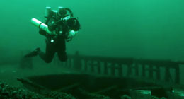 Underwater archeaologist diving underwater to examine a historic shipwreck.