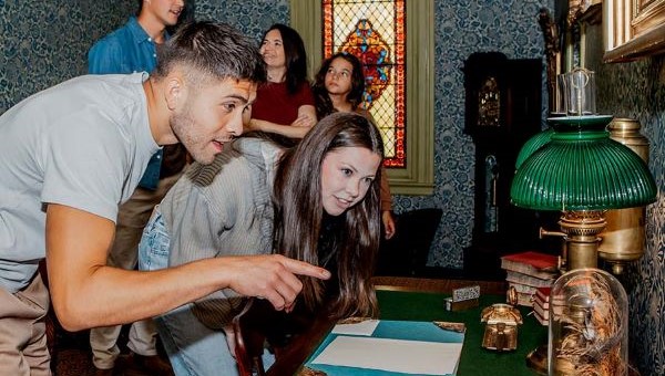 A man and a woman lean over a table to look at an object as the man points to it.