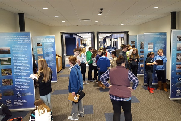 Students take notes on an exhibit set up in a school hallway.