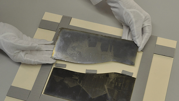 Image of someone wearing white protective gloves as they piece two halves of an historic image together