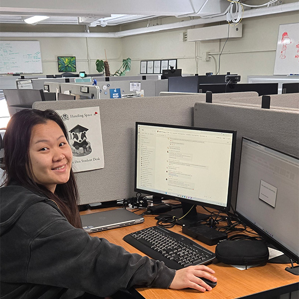 Young woman with long dark hair sits at a computer smiling