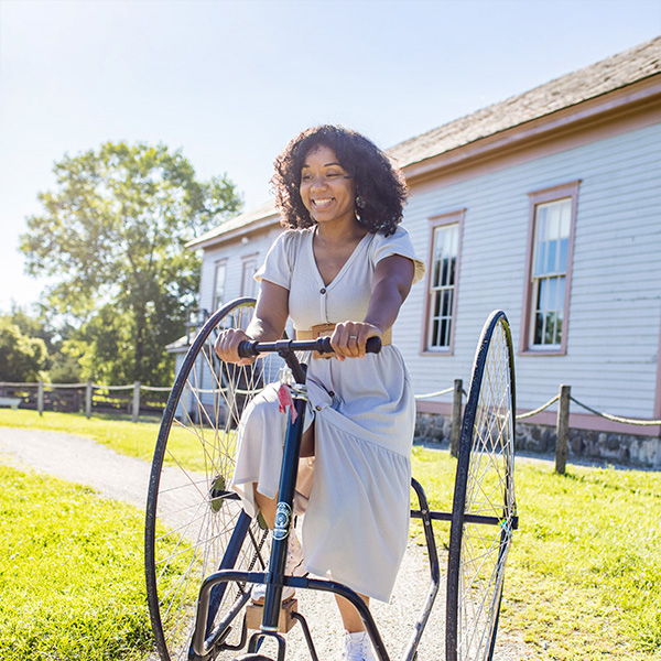 A woman smiling while riding a large bicycle at Old World Wisconsin