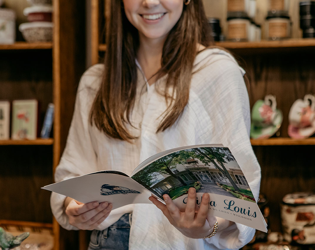 A light-complected woman with brown hair smiles and looks at a magazine about Villa Louis.