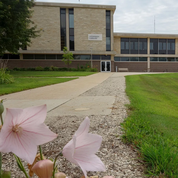 The UW Whitewater Andersen library. Pink flowers bloom near the sidewalk leading up to the library entrance.