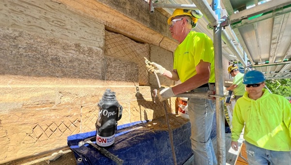 Two construction workers in yellow work on scaffolding restoring an old building