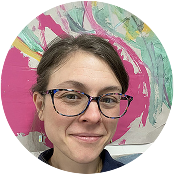 Headshot of Abby Pfisterer with finger paintings in the background, she has dark brown hair and wears dark glasses