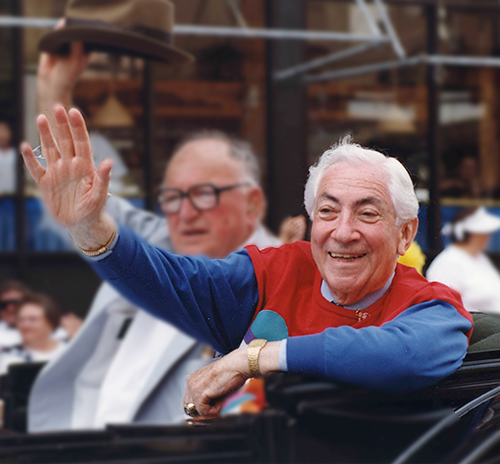 WHI ID #3701 Ben Barkin rides in a vintage convertible waving happily to the crowd during a parade. His shirt is bright red and blue color block.