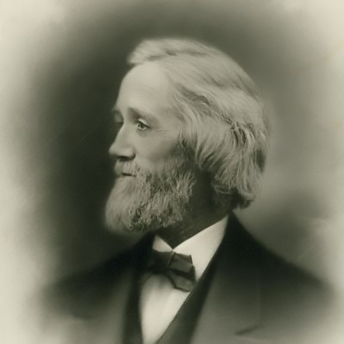 C. Latham Sholes in his later years. Looking away from the camera in this formal studio portrait, he stares hard to the left his hair and beard full and white, in a smart suit and bowtie.