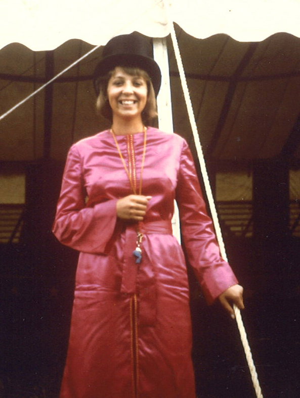 Photo Credit: Circus World Museum Elizabeth Fentress wears a bright magenta floor length satin gown. She smiles proudly in her top hat directly facing the camera in front of the big top circus.