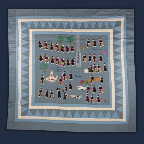 Hand stitched journey quilt with a grey and periwinkley triangle border and straight borders. The interior depicts many brightly colored figures depicting the Secret War in Laos and the Hmong escape across the Mekong River and journeying to the U.S.A., made by Ge Yang.