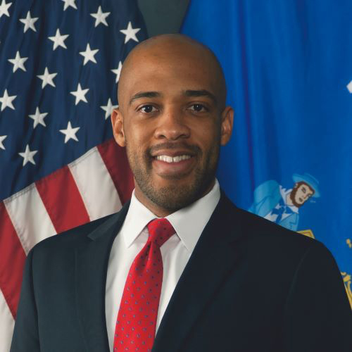 Lieutenant Governor Mandela Barnes smiles proudly at the camera in this portrait in front of the Wisconsin & US Flags