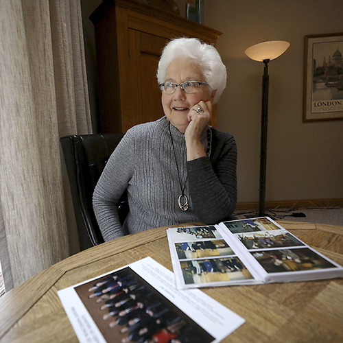 Margaret Farrow, Wisconsin’s first female lieutenant governor, at her home in Pewaukee. She looks off to the left away from the camera her hand on her chin smiling and looking as though she might be remembering the past, photos spread before her.