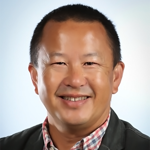 A formal headshot of Pao Lor, head on smiling at the camera wearing a red and white checkered collard shirt under a black jacket. He smiles happily at the camera, his black hair cropped close.