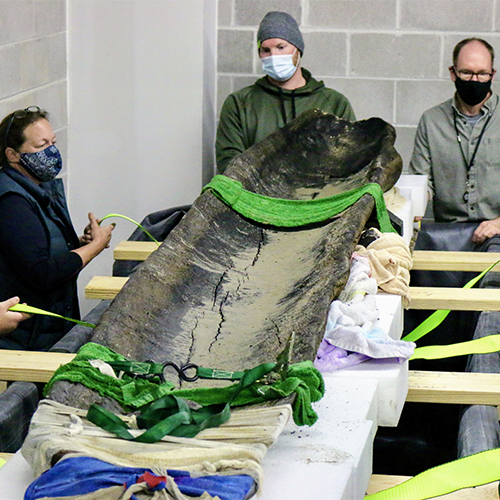 3 staff members from the Wisconsin Historical Society showcase the canoe recently unearthed from Lake Mendota.