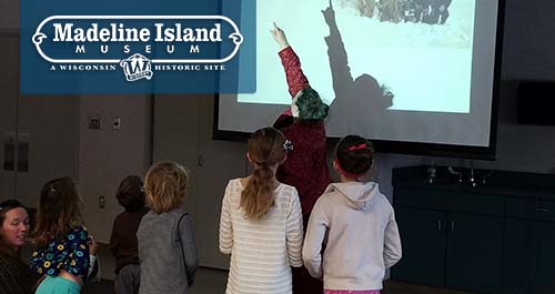 Madeline Island Museum. Kids look on as a instructor points things out on a projector.