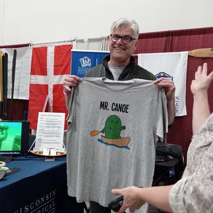 Jim smiles animatedly over a t-shirt reading 'Mr. Canoe'