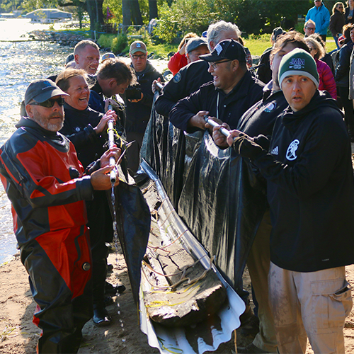 The team joyously carries the canoe across the beach, Tamara Thompsen and Bill Quackenbush (Ho-Chunk Tribal Preservation Officer) share a laugh.