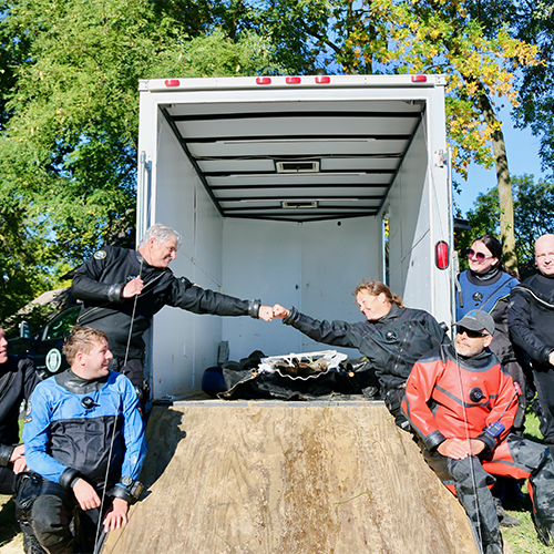 Tamara Thomsen and Jim Skibo bump fists in front of the safely collected canoe in the truck, team poses around them.