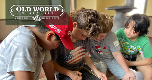 Old World Wisconsin. Kids huddle around a slate writing like settlers did.