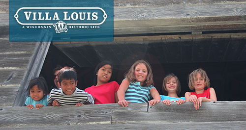 Villa Louis. A group of children hang out of a window of a rustic looking builing, smiling down at the camera