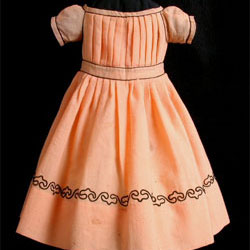 Image of a girl's dress that is pale orange wool with black soutache trim dating to 1865.