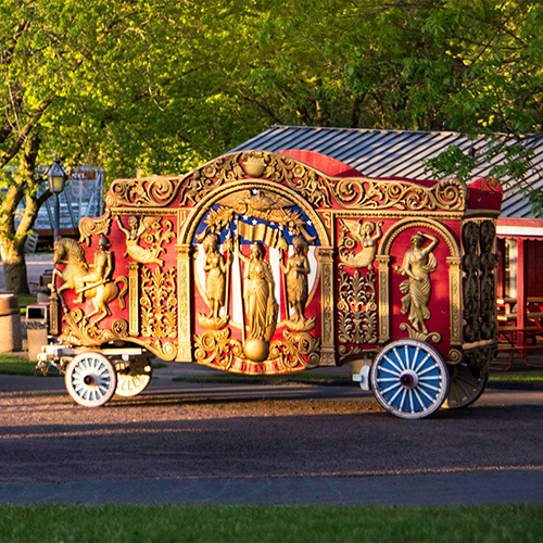 A circus cart on a lawn, bright red, yellow, and orange colors.