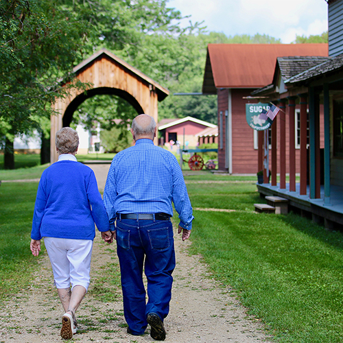 A older white couple holding hands and walking towards the Stonefield buildings